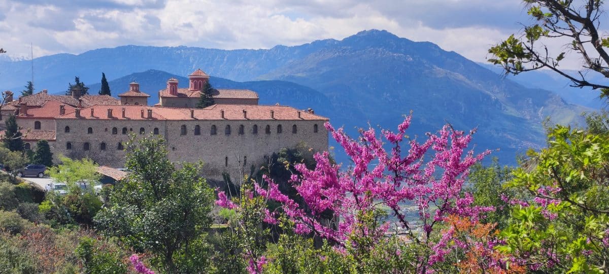 Photographie des Météores en Grèce, avec un arbre rose au premier plan et un monastère en arrière-plan, représentant "6 Destinations pour un Premier Voyage Solo"