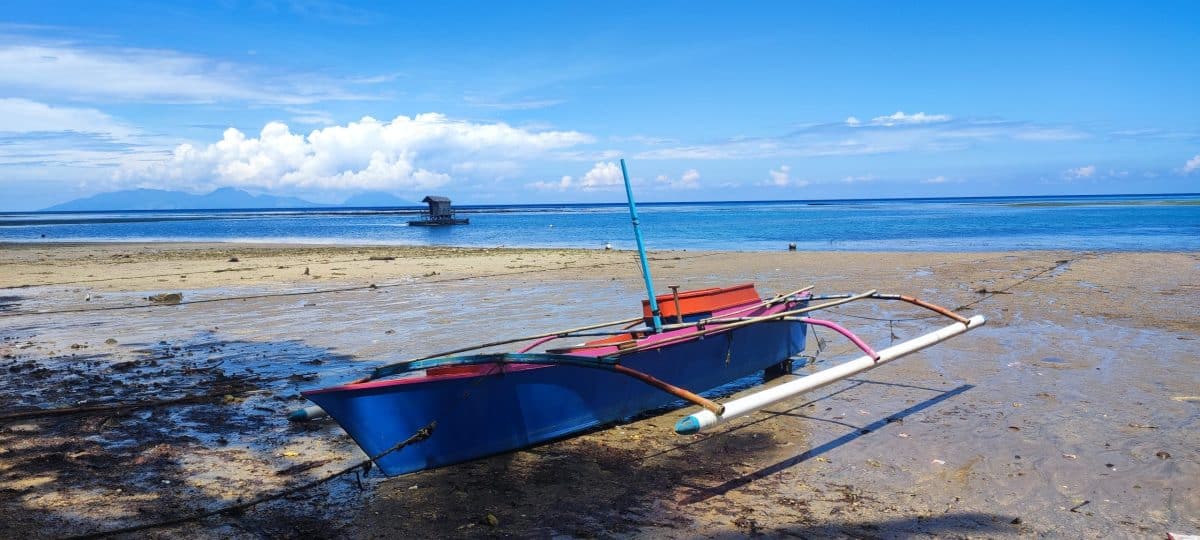 Bateau de pêcheur bleu et rouge échoué sur le sable de l'île de Siau, Sulawesi