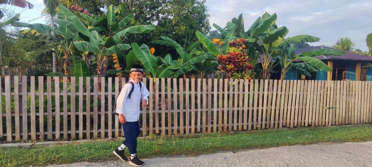 Un enfant souriant de l'île de Siau, Sulawesi, pose devant une barrière en bois, exprimant la joie et l'innocence de l'enfance