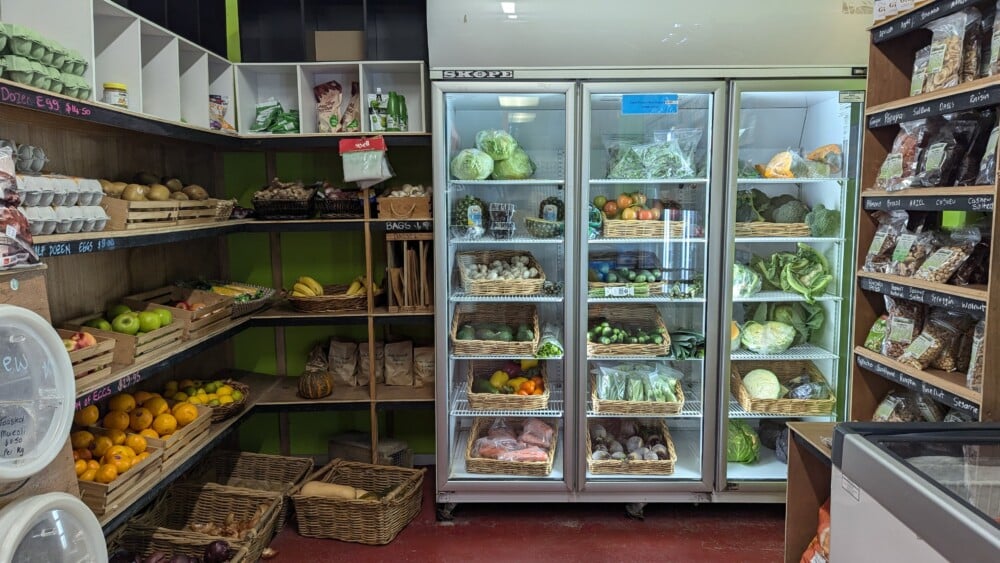 Photo de l'intérieur d'une épicerie à Claris, montrant des légumes dans un réfrigérateur et sur une étagère