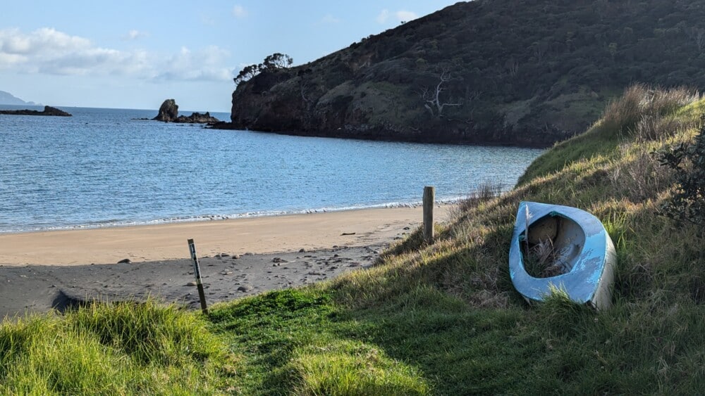 Photo d'un paysage de l'île de la Grande Barrière, avec une plage, un canoë, de l'herbe derrière la plage et la mer