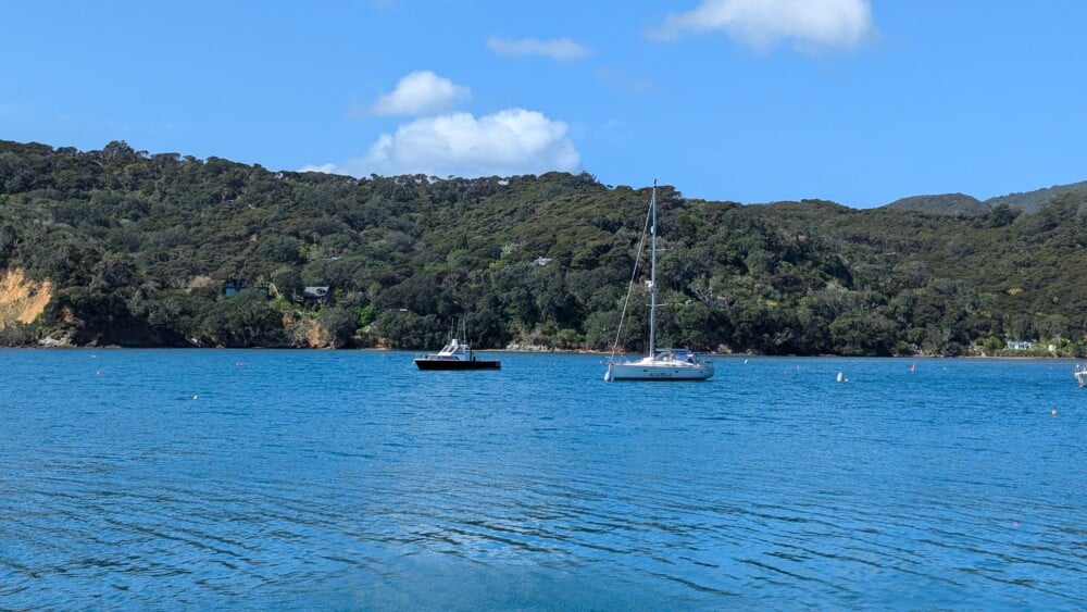 Photo d'un paysage de l'île de la Grande Barrière, avec un bateau bleu sous un ciel bleu