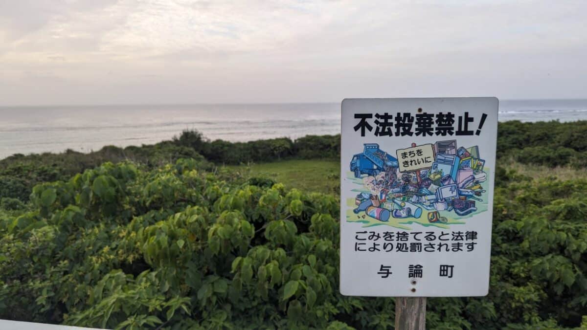 Panneau écologique blanc à Yoron Island, Japon, avec photo de détritus et texte noir. Environnement naturel avec arbres et mer en arrière-plan