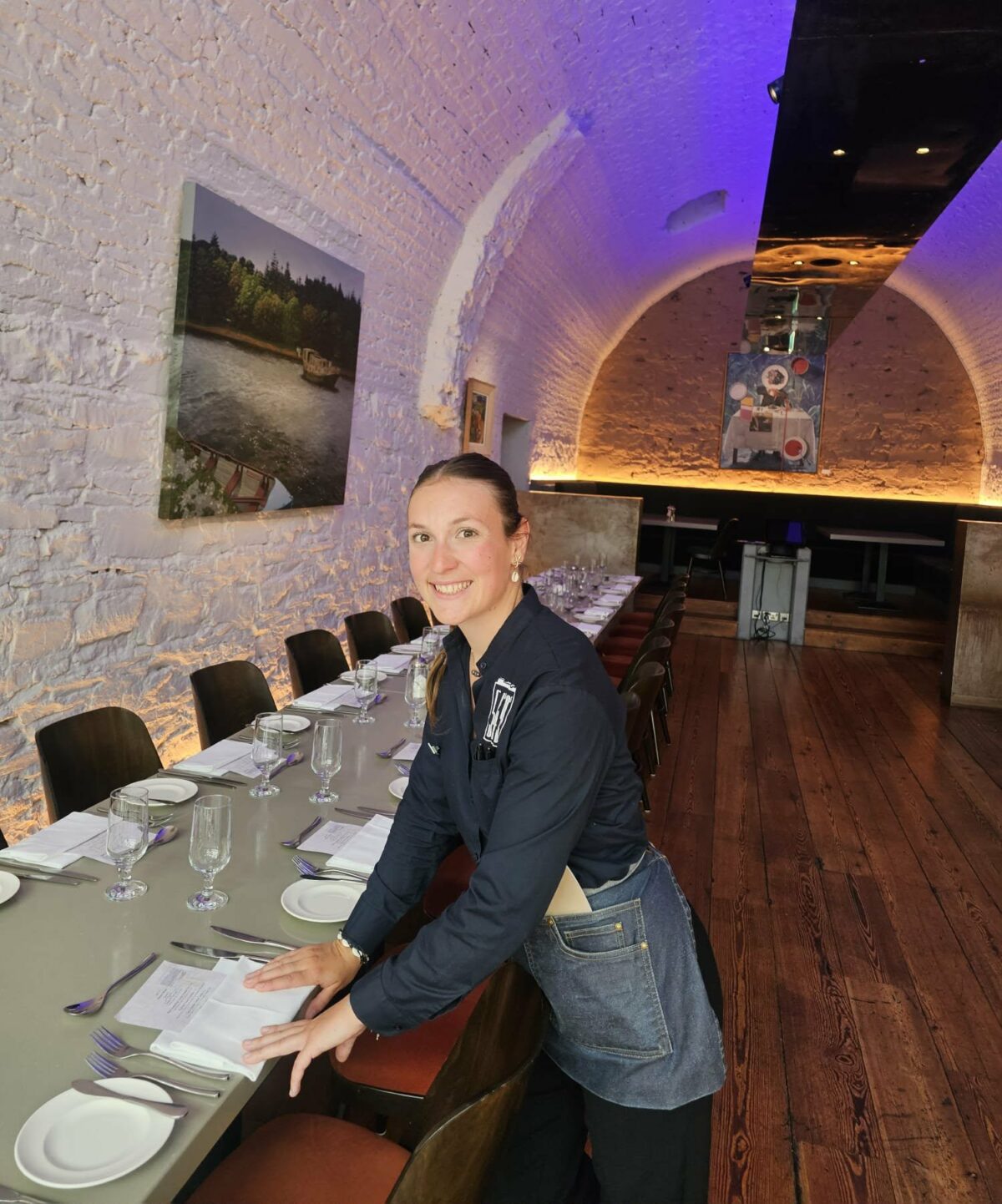 Fanny souriante au service client, debout à côté d’une table dans un grand restaurant, lors de ses voyages en Irlande et en Asie du Sud-Est. Illustration qui capture l’accueil chaleureux, la convivialité et l’expérience du travail ou de la rencontre dans la restauration