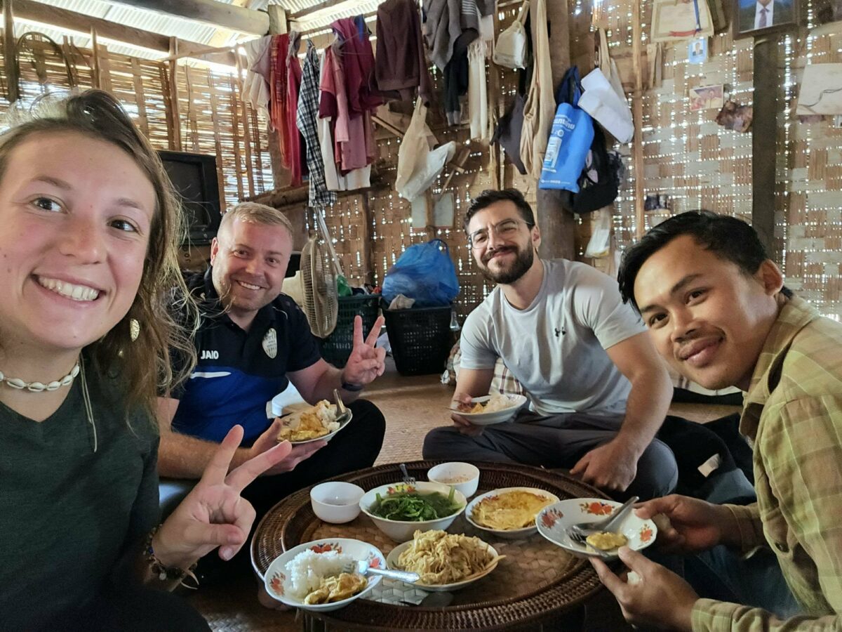Selfie de groupe avec Fanny et deux autres personnes, Fanny en train de goûter de la nourriture locale d’Asie du Sud-Est, style Vietnam. Illustration qui capture le partage, la convivialité et la découverte culinaire pendant le voyage