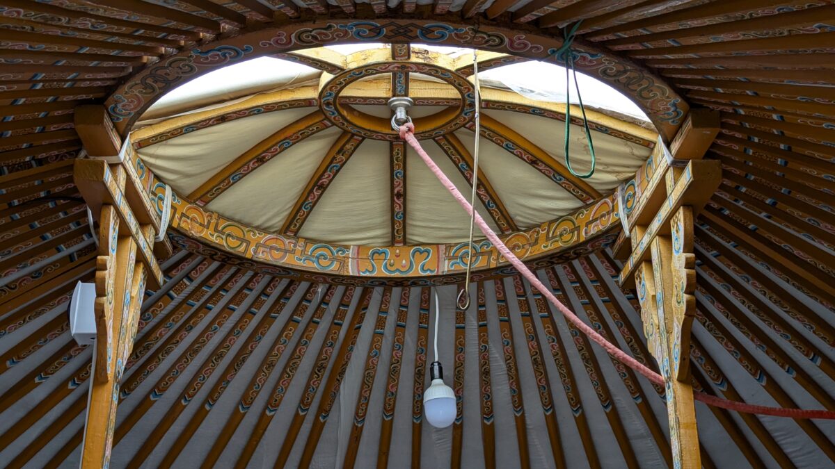 Intérieur d’une yourte en Mongolie avec structure circulaire en bois. Lumière suspendue au centre sous le toit, ambiance chaleureuse et nomade