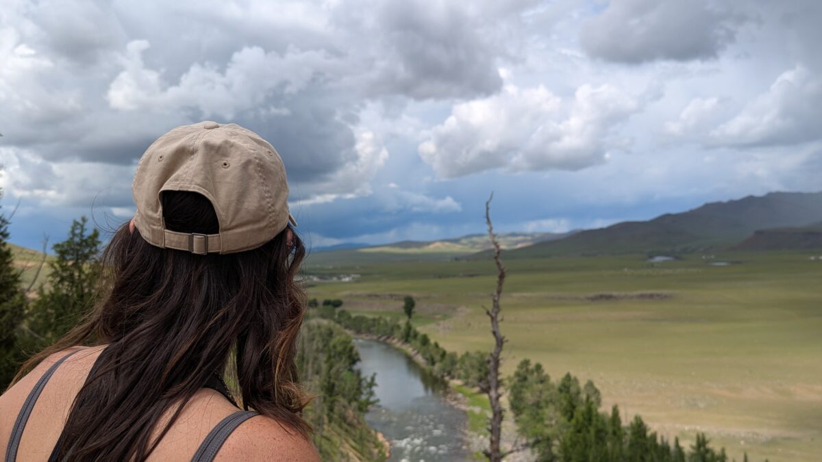 Inès vue de dos avec une casquette, contemplant la vallée de l’Orkhon en Mongolie. Elle regarde vers la rivière en contrebas dans un vaste paysage naturel