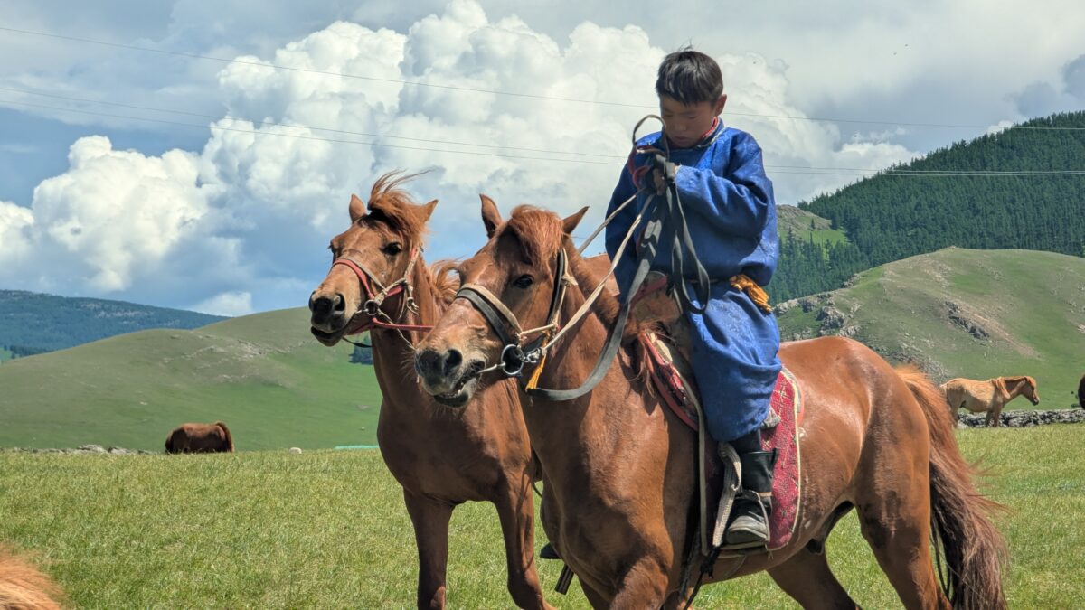 Jeune nomade en Mongolie à cheval dans la steppe, tenant un second cheval par la bride. Portrait de vie nomade en pleine nature, entre liberté et immensité des paysages