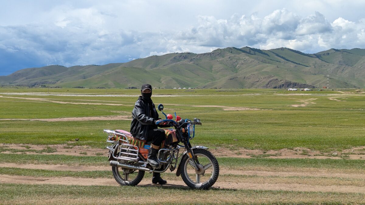 Jeune garçon assis sur une moto dans la steppe mongole. Paysage ouvert avec montagnes en arrière-plan