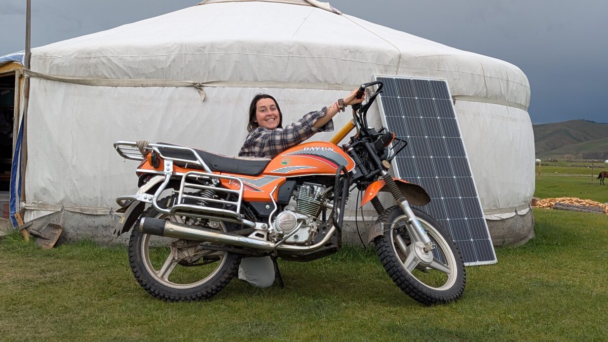 Inès debout à côté de sa moto lors d’un voyage en mode nomade en Mongolie. Scène de voyage solo dans les steppes mongoles, entre liberté et aventure
