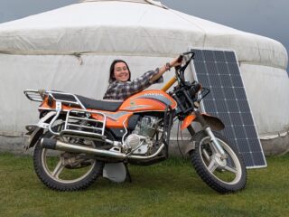 Inès debout à côté de sa moto lors d’un voyage en mode nomade en Mongolie. Scène de voyage solo dans les steppes mongoles, entre liberté et aventure