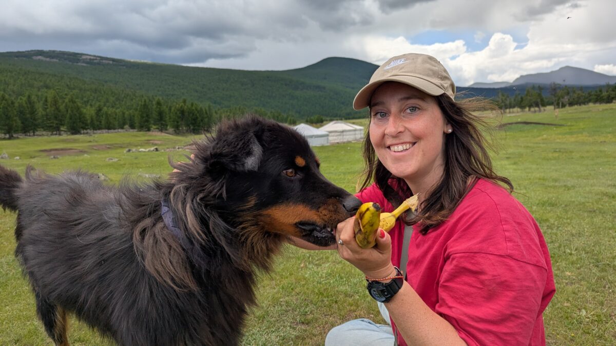 Inès souriante dans un campement nomade en Mongolie avec un chien à ses côtés. Ambiance chaleureuse au cœur de la vallée de l’Orkhon