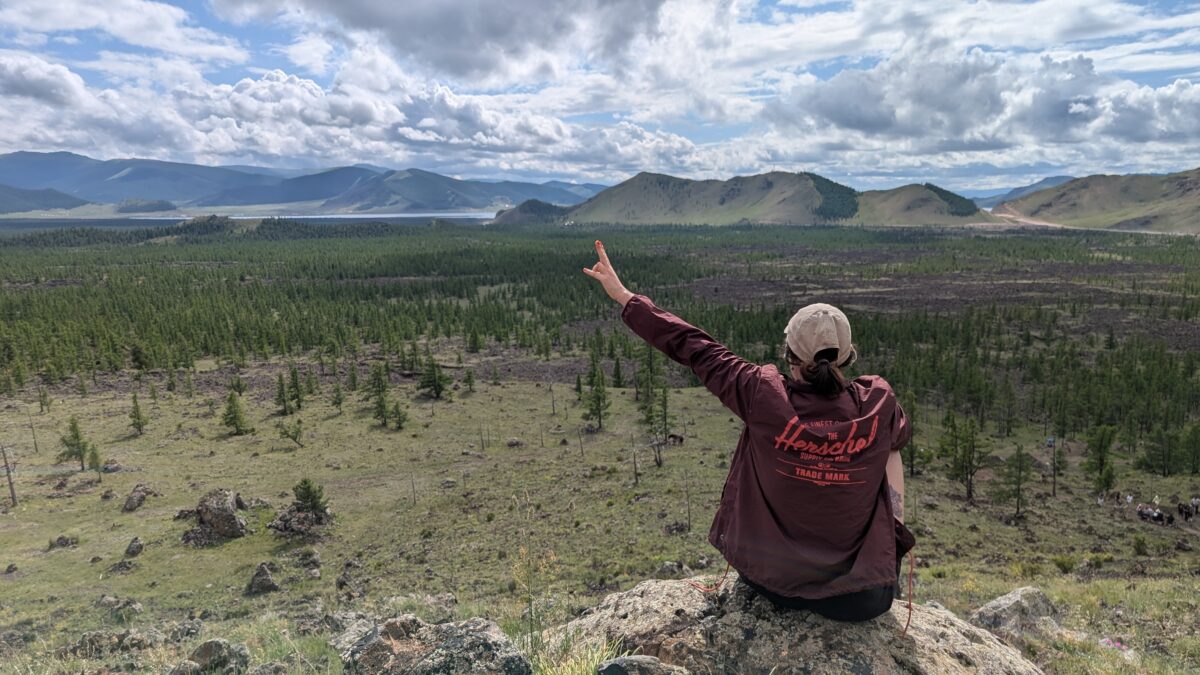 Inès de dos, bras levés face à un paysage volcanique en Mongolie. Scène d’immensité naturelle et de contemplation