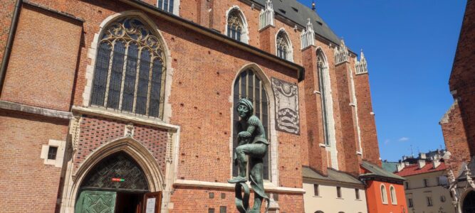 Statue d'un travailleur devant la basilique Sainte-Marie à Cracovie, avec des murs en brique rouge