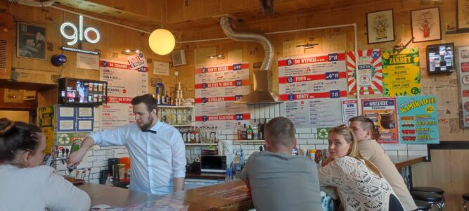 Un serveur en chemise sert des clients dans un bar à vodka à Cracovie, entouré de touristes au comptoir