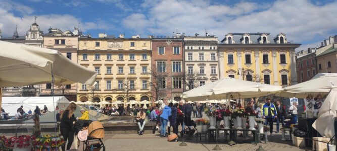 Rynek Główny à Cracovie, avec des maisons colorées, des parasols et des passants