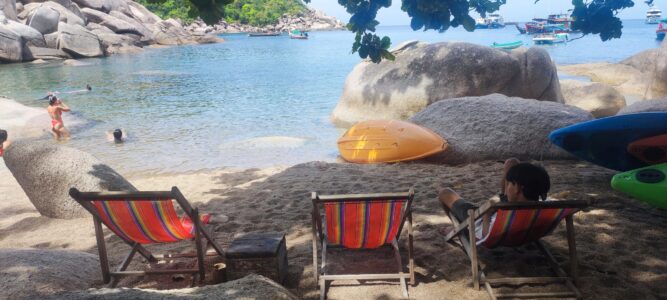 Transats rouges alignés sur la plage de Koh Tao, avec un bateau en arrière-plan et des eaux bleu turquoise
