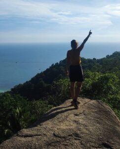 Inès, une aventurière à Koh Tao, levant les bras de dos devant une vue panoramique sur la mer