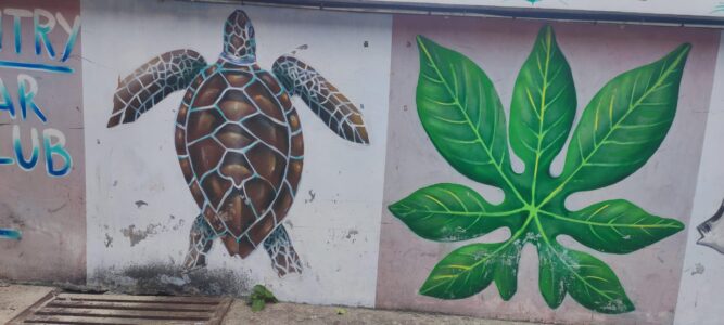 Un local posant avec un sourire devant une œuvre de street art colorée à Koh Tao, illustrant la culture vibrante de l'île