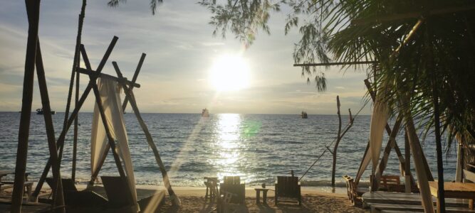 Plage de Koh Tao avec des transats sous des palmiers, et le soleil encore haut dans le ciel bleu clair, illuminant la mer tranquille