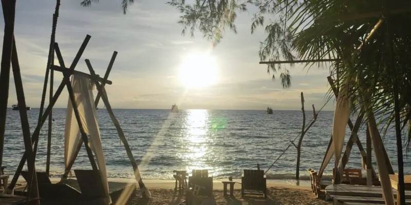 Plage de Koh Tao avec des transats sous des palmiers, et le soleil encore haut dans le ciel bleu clair, illuminant la mer tranquille
