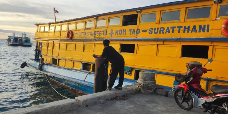 Un homme attend avec son scooter devant un bateau de transport jaune à Koh Tao
