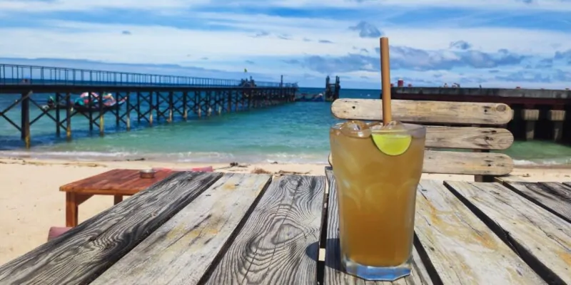 Une boisson colorée posée sur une table, avec une vue sur la plage de Koh Tao et des eaux turquoise en arrière-plan