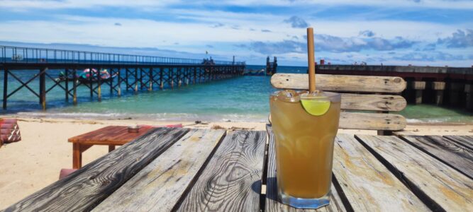 Une boisson colorée posée sur une table, avec une vue sur la plage de Koh Tao et des eaux turquoise en arrière-plan