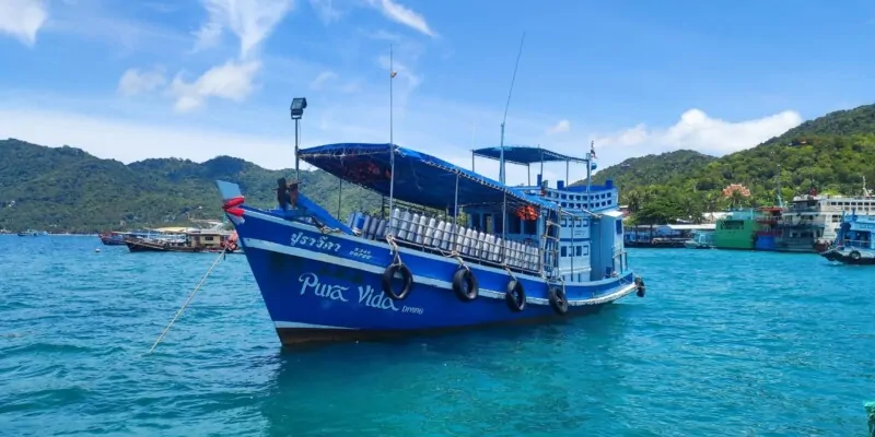 Bateau de plongée naviguant dans les eaux turquoise de Koh Tao, avec des montagnes verdoyantes en arrière-plan