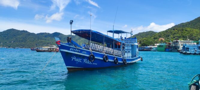 Bateau de plongée naviguant dans les eaux turquoise de Koh Tao, avec des montagnes verdoyantes en arrière-plan