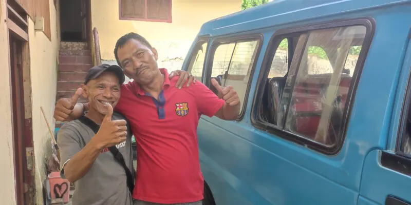 Portrait d'un conducteur de Manado faisant un geste de pouce en l'air à côté d'un bemo bleu