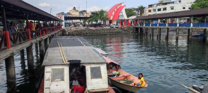 Photographie du port de Manado avec des bateaux locaux en route vers Bunaken, incluant une jeune fille dans une barque