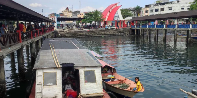 Photographie du port de Manado avec des bateaux locaux en route vers Bunaken, incluant une jeune fille dans une barque
