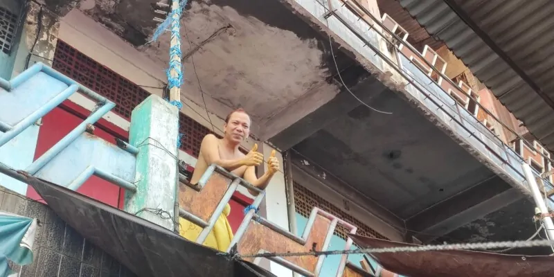 Portrait d'un homme torse nu à Manado faisant un geste de pouce en l'air depuis son balcon