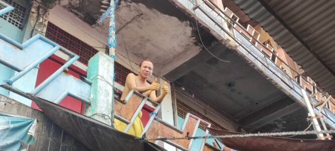 Portrait d'un homme torse nu à Manado faisant un geste de pouce en l'air depuis son balcon