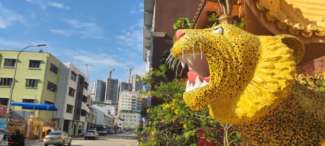 Photographie d'un temple chinois à Singapour, mettant en avant une tête de lion dorée avec la rue animée en arrière-plan