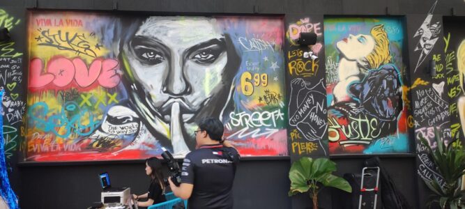 Photographie de street art à Singapour, représentant une femme faisant un geste de "chut" avec son doigt, tandis qu'un homme se tient devant