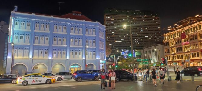 Photographie de Singapour de nuit, montrant des bâtiments modernes illuminés et des passants dans les rues animées