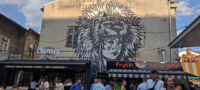 Œuvre de street art d'une femme à tête de lion au Judah Food Market dans le quartier juif de Cracovie, avec des food trucks et des gens en train de manger