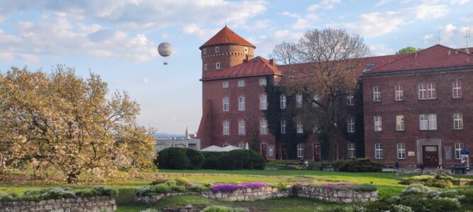 Le Château de Wawel à Cracovie, entouré de jardins verdoyants, avec des murs rouges et un ballon coloré flottant dans le ciel