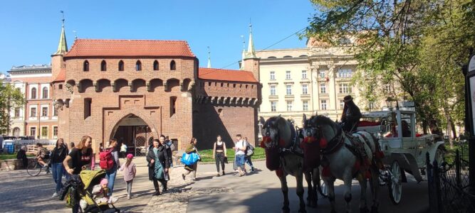 Touristes devant le Barbacane de Cracovie, avec une calèche tirée par un cheval stationnée à proximité