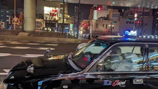 Dotonbori à Osaka illuminé la nuit, avec ses néons colorés et son ambiance vibrante, où un taxi noir emblématique se dirige vers le quartier animé