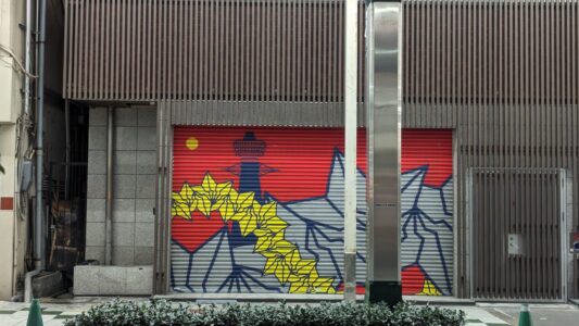 Street art de la tour Tsutenkaku Mural de street art représentant la tour Tsutenkaku à Osaka, peint en rouge et jaune sur la porte d'un parking