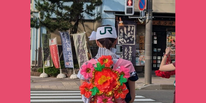 Jeune femme de dos portant un habit traditionnel d'Aomori et un chapeau marqué du logo JR
