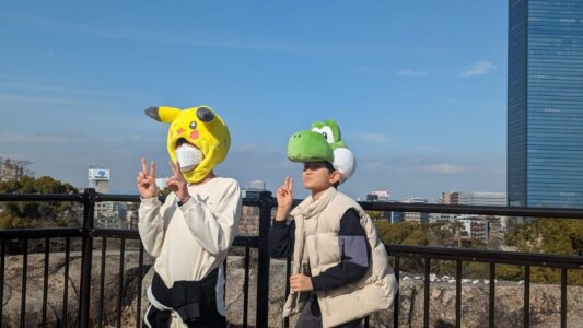 Deux jeunes portant des masques de Pikachu et Yoshi se tenant devant le parc du Château d'Osaka