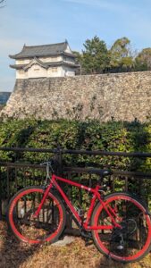 Vélo rouge garé devant le Château d'Osaka, entouré de jardins et d'arbres