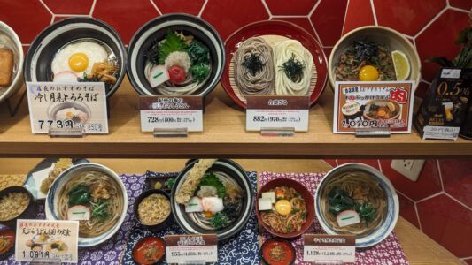 Udon & Tempura Image d'une vitrine d’un restaurant à Osaka, exposant des répliques de plats d'udon, soba, et autres spécialités culinaires, typiques de la street food japonaise