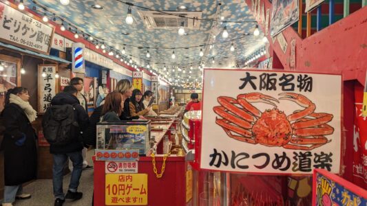 Grande statue de crabe des neiges à Shinsekai, Osaka, entourée de visiteurs japonais admirant la spécialité locale