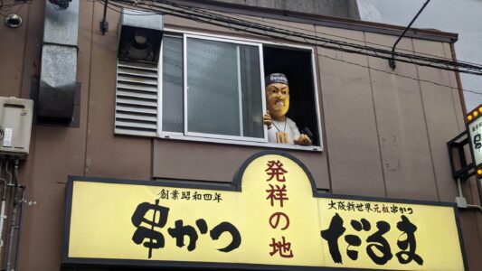Figure emblématique à Shinsekai, Osaka, vue à travers une fenêtre, illustrant l'animation du quartier