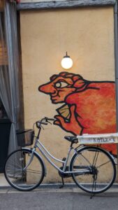 Street Art la sorcière de Chihiro ? Fresque murale de style néo-grunge représentant un vélo avec une sorcière et des éléments du voyage de Chihiro à Osaka